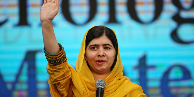 Foto de Malala discursando, uma menina de cabelos pretos, olhos pretos e um xale amarelo com uma mão levantada